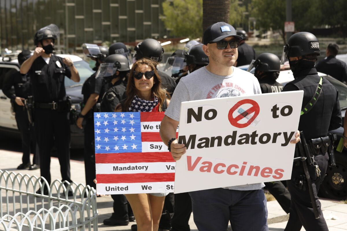 A man and woman against vaccine mandates hold signs while police walk behind them.