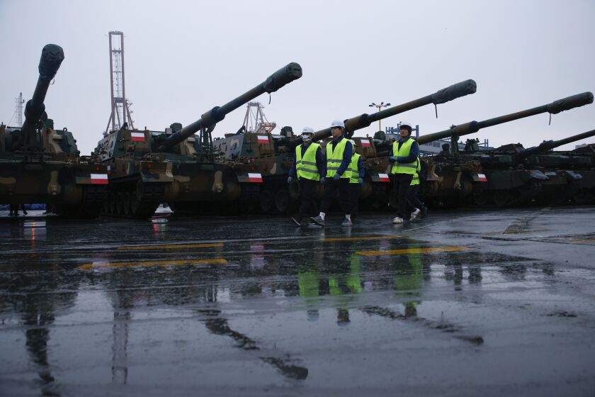 South Korea delegation walks next to the Thunder K9 howitzers in the Polish Navy port of Gdynia, Poland, Tuesday, Dec. 6, 2022. Poland's President Andrzej Duda and the defense minister on Tuesday welcomed the first delivery of tanks and howitzers from South Korea, hailing the swift implementation of a deal signed in the summer in the face of the war in neighbouring Ukraine. (AP Photo/Michal Dyjuk)