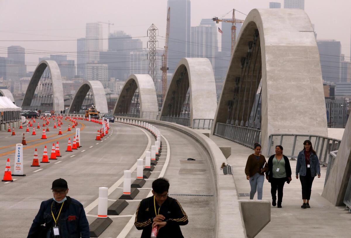 People are seen walking on a bridge bordered by multiple arches.