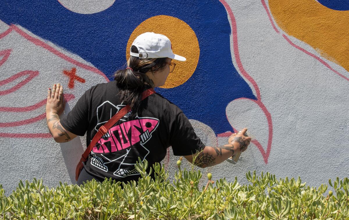 Long Beach Walls artist Stevie Shao sprays paint on a mural in progress on a building at the Renaissance High School