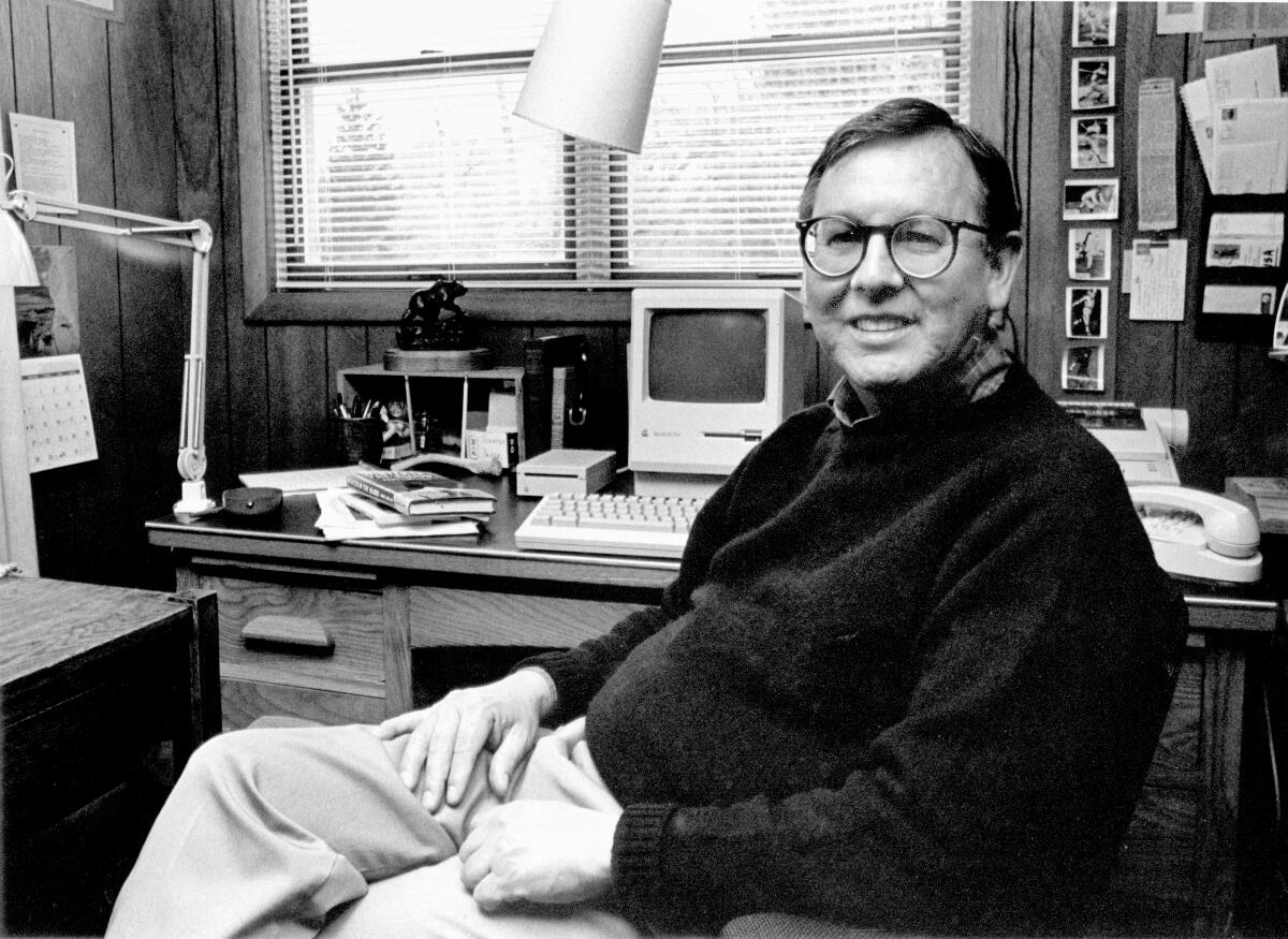 A smiling man sitting in a chair at a desk. 