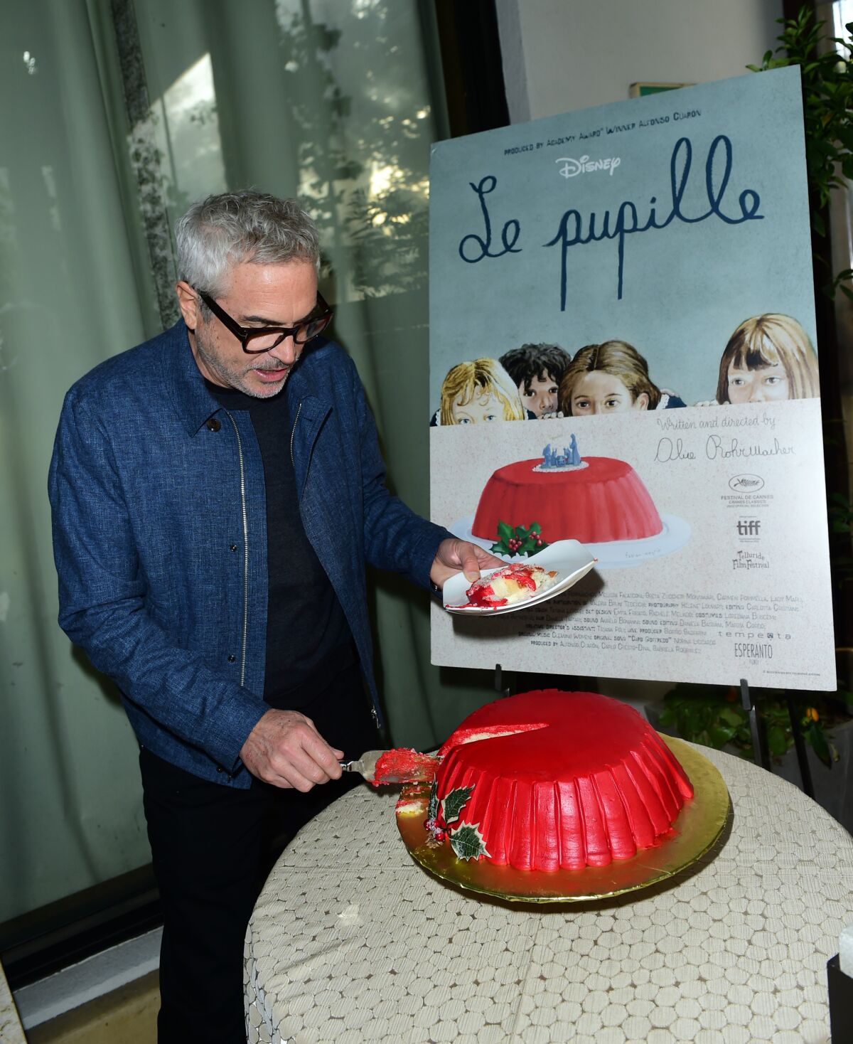 Director Alfonso Cuarón takes a slice of cake beneath a poster for the short film "Le Pupille."
