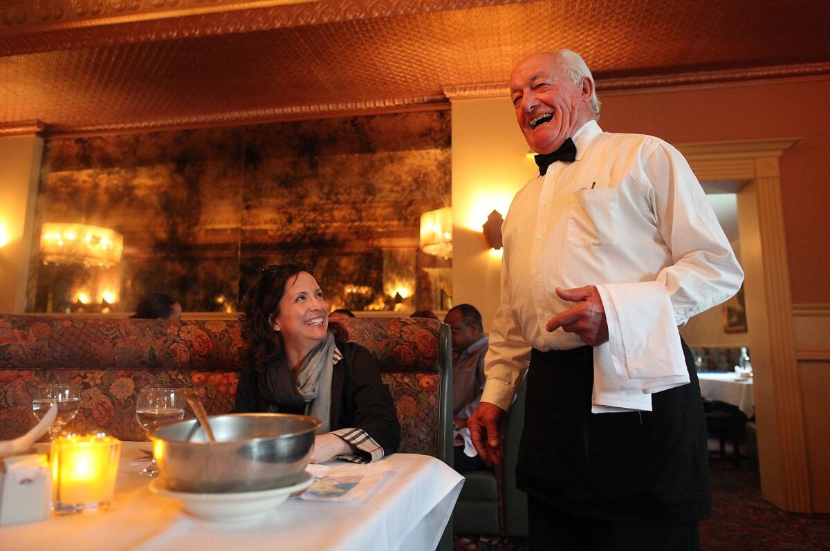 A woman sits at a restaurant table and smiles with a waiter