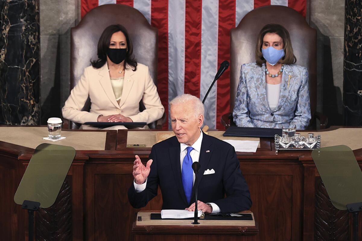 President Biden speaks at a lectern with Kamala Harris and Nancy Pelosi sitting behind him