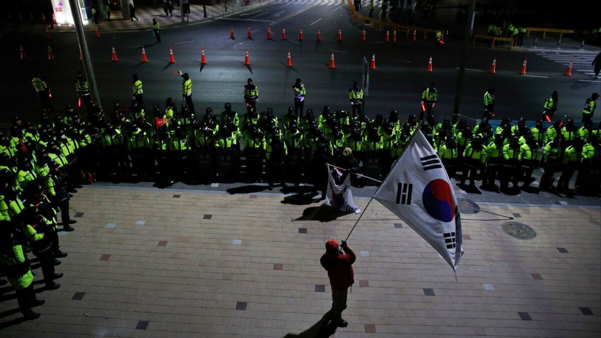 A protester holds a large South Korean flag as he is surrounded by police officers during a rally outside the Gangneung Arts Center, where North Korea's Samjiyon art troupe performed, ahead of the 2018 Winter Olympics in Gangneung, South Korea on Feb. 8.