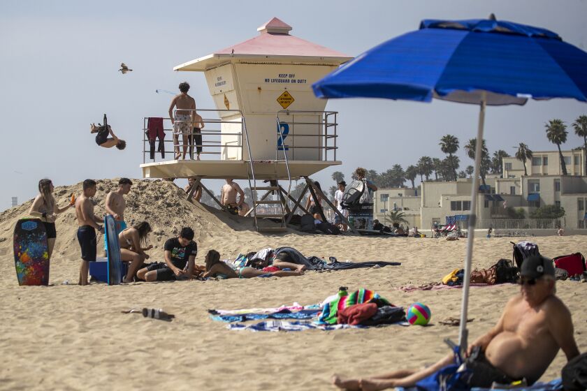 HUNTINGTON BEACH, CA -- THURSDAY, APRIL 30, 2020: Kids do flips off the lifeguard tower while others relax on the sand on the last day of open beaches in Huntington Beach after Gov. Newsom announced the "hard close" of all Orange County state and local beaches Thursday, April 30, 2020. Newsom's retaliation came after thousands of Californians flocked to the shoreline there over the weekend in defiance of a statewide stay-at-home order enacted to stem the spread of the coronavirus. "When you contact the police chiefs to enforce your will as a leader-in my book you establish a police state" said Huntington Beach resident Pete Hamborg. "It's a moment that Gavin Newsom is taking away from us and are the very moments that empower us to deal with this crisis on a day-to-day basis." "I think the beach, which belongs to all Californians, is critical to our emotional health and well-being." (Allen J. Schaben / Los Angeles Times)