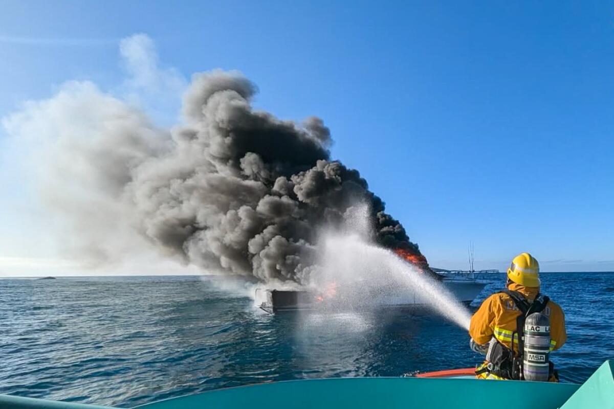 A firefighter sprays water on a burning boat.