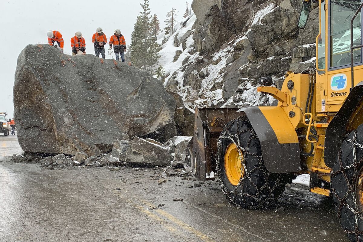 In this photo provided by Caltrans, a crew places explosives into a large boulder that fell onto U.S. Highway 50 near South Lake Tahoe, Calif., Friday, March 4, 2022. The return of winter weather prompted forecasters to advise people planning mountain travel to be prepared for snowy roads Friday and Saturday. Travel through the Sierra was disrupted by the massive boulder that fell onto the highway at Echo Summit on Thursday. (Caltrans via AP)