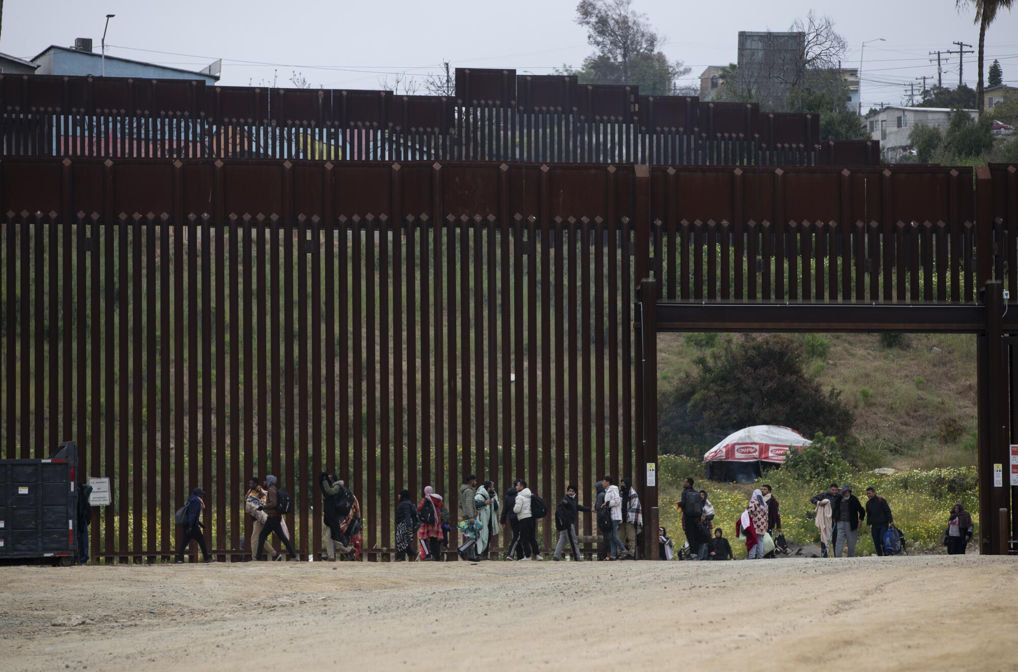 Dozens of asylum-seeking migrants run out of an open gate before being stopped by U.S. Border Patrol agents.