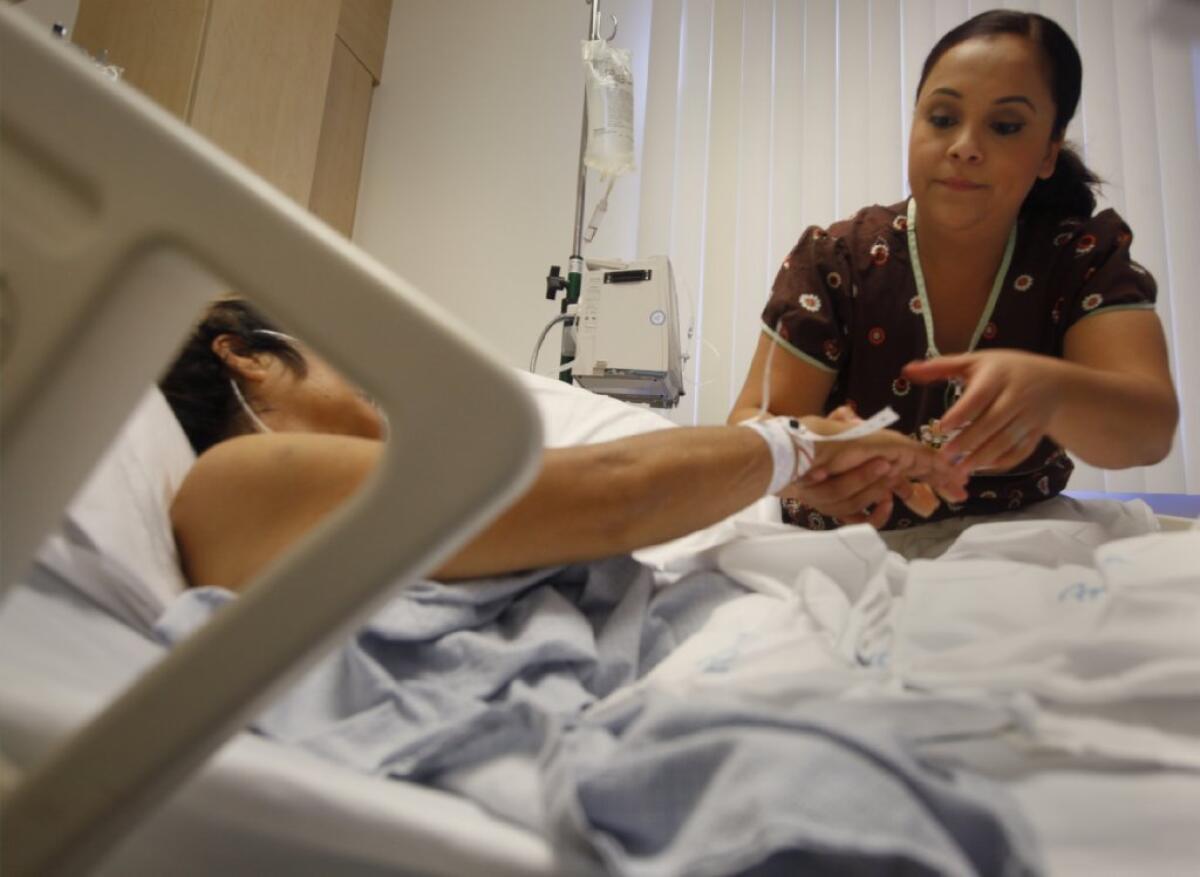 Many nurses like Sherlyn Ocampo, pictured here in January tending to a patient at Downey Regional Medical Center, already get immunized against the flu to protect patients and themselves. Now all healthcare workers in Los Angeles County will be required to get a flu shot, or wear a face mask.