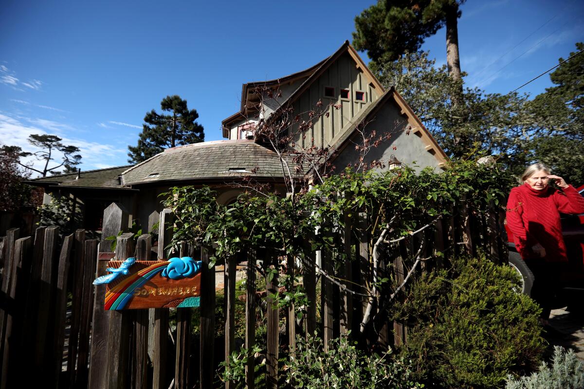 A woman stands in front of a gabled house in Carmel-by-the-Sea. 