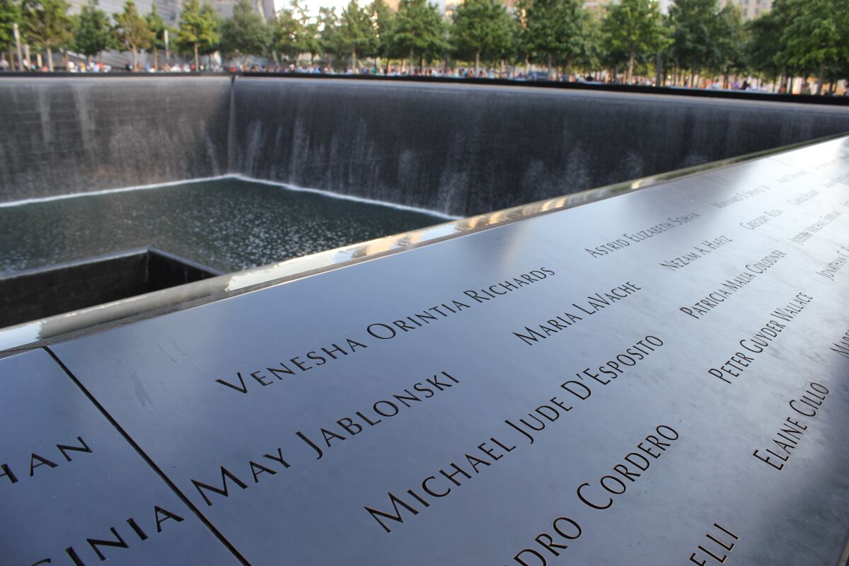 A black panel bearing the names of the dead is seen in the foreground of one of the memorial pools.