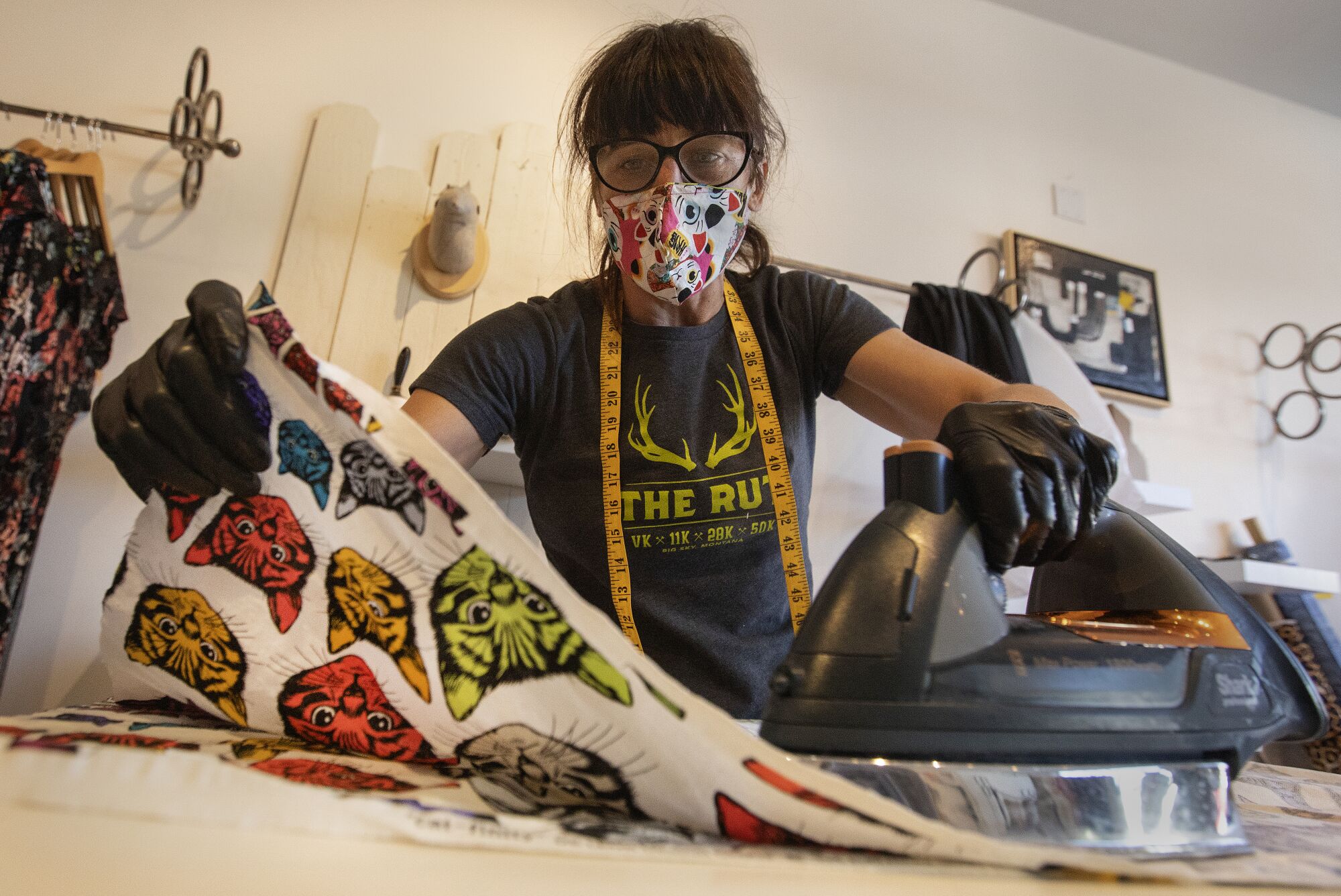 Laura Howe irons the creases out of scraps from fabric, originally used to make dresses, that is now being used to make masks at her store in Silver Lake.