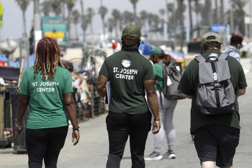 People in T-shirts that say "St. Joseph Center" walk along a street.