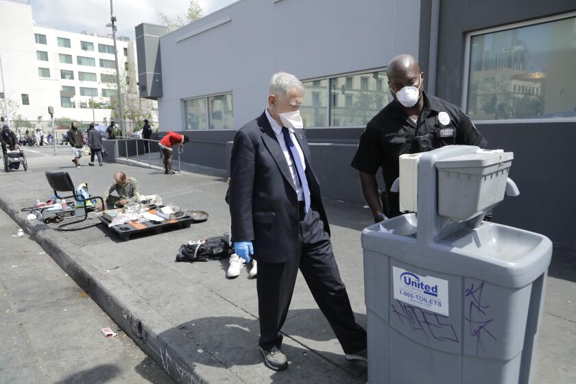 LOS ANGELES, CA - APRIL 03: U.S. District Court judge David O. Carter and LAPD officer Deon Joseph check an empty water dispenser while touring skid row on Friday, April 3, 2020 in Los Angeles, CA. Officer Joseph said he noticed it empty about 1 1/2 weeks ago. Carter is the judge at the center of the Orange County riverbed homeless case. (Myung J. Chun / Los Angeles Times)