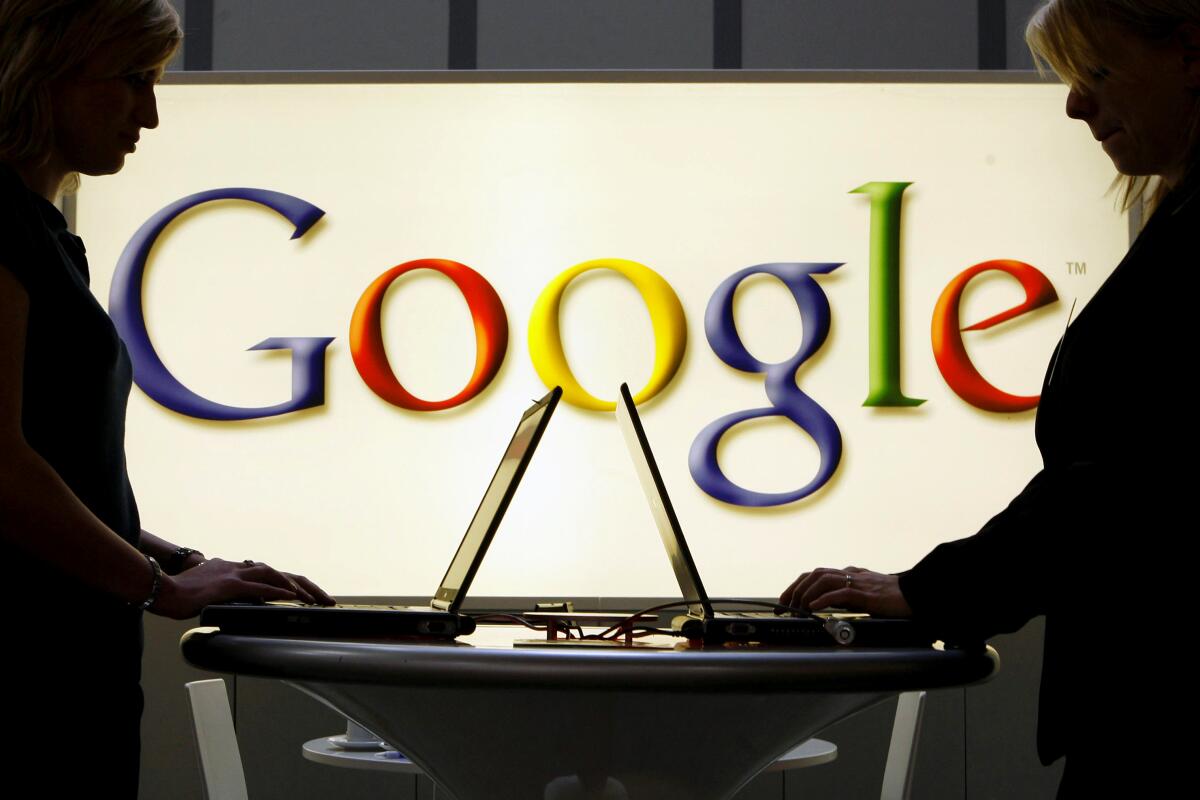 In this April 17, 2007 file photo, exhibitors work on laptop computers in front of an illuminated sign of the Google logo 