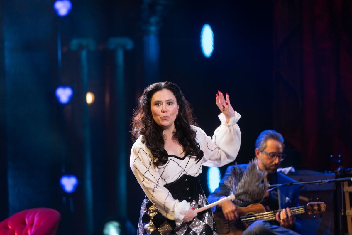 A woman in period costume holding a drumstick on stage.