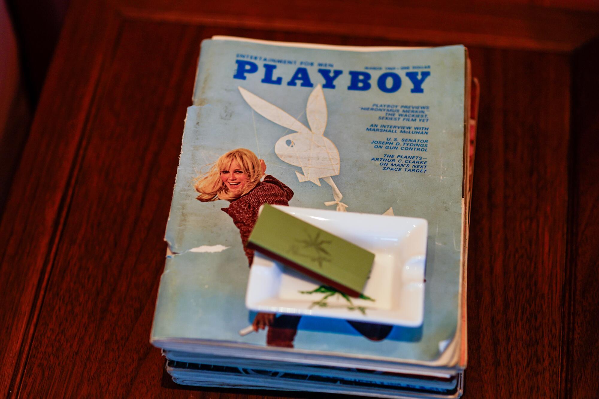 An ashtray and pack of matches  atop a stack of Playboy magazines
