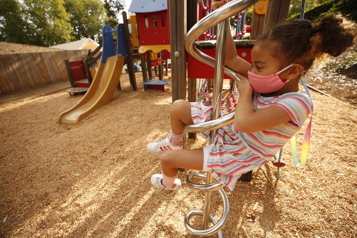 A kindergartener wears a face mask while on playground equipment