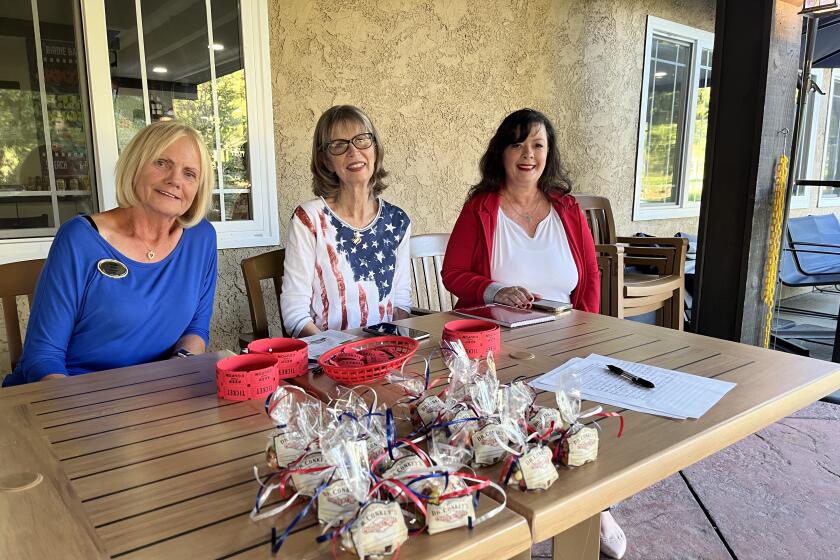 Three women in red, white and blue sit behind a table with baggies of jelly beans. 