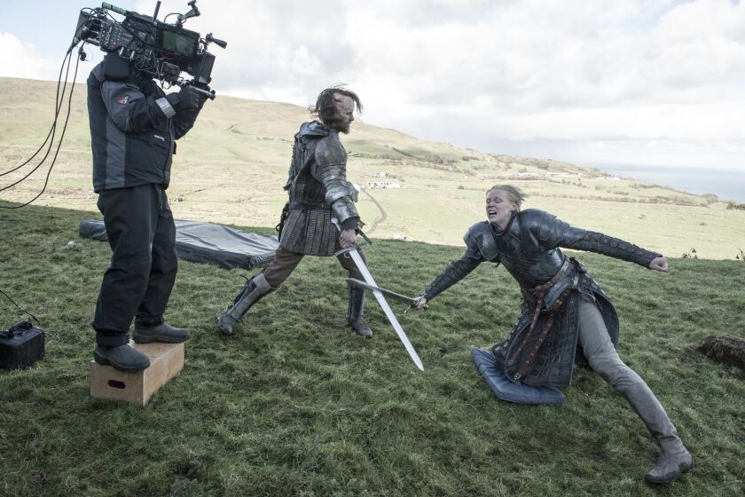 On location in the countryside of Northern Ireland, a GOT cameraman photographs a sword fight scene between Rory McCann, center, and Gwendoline Christie.
