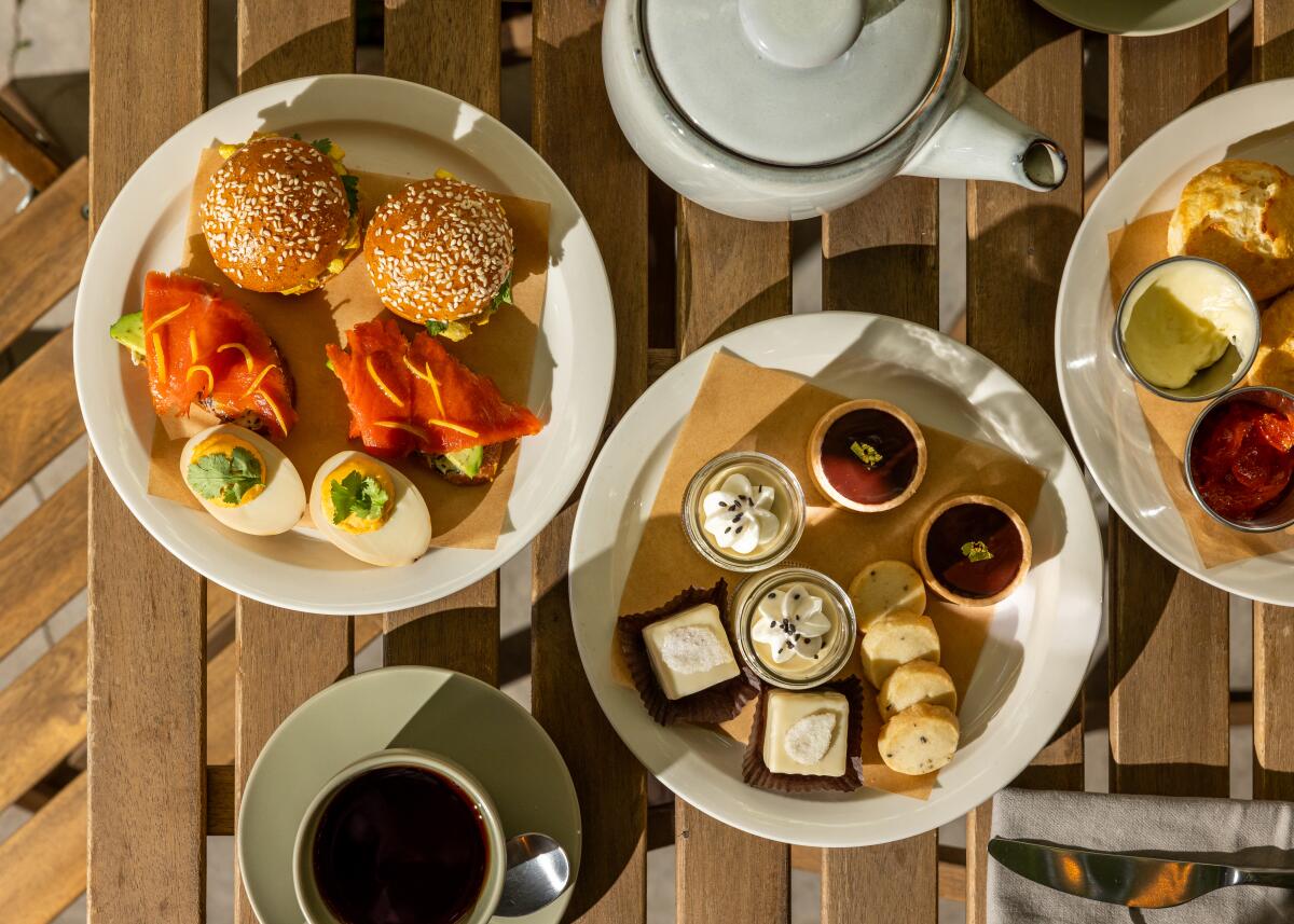 A high tea set of pastries, sandwiches and hardboiled eggson a table.