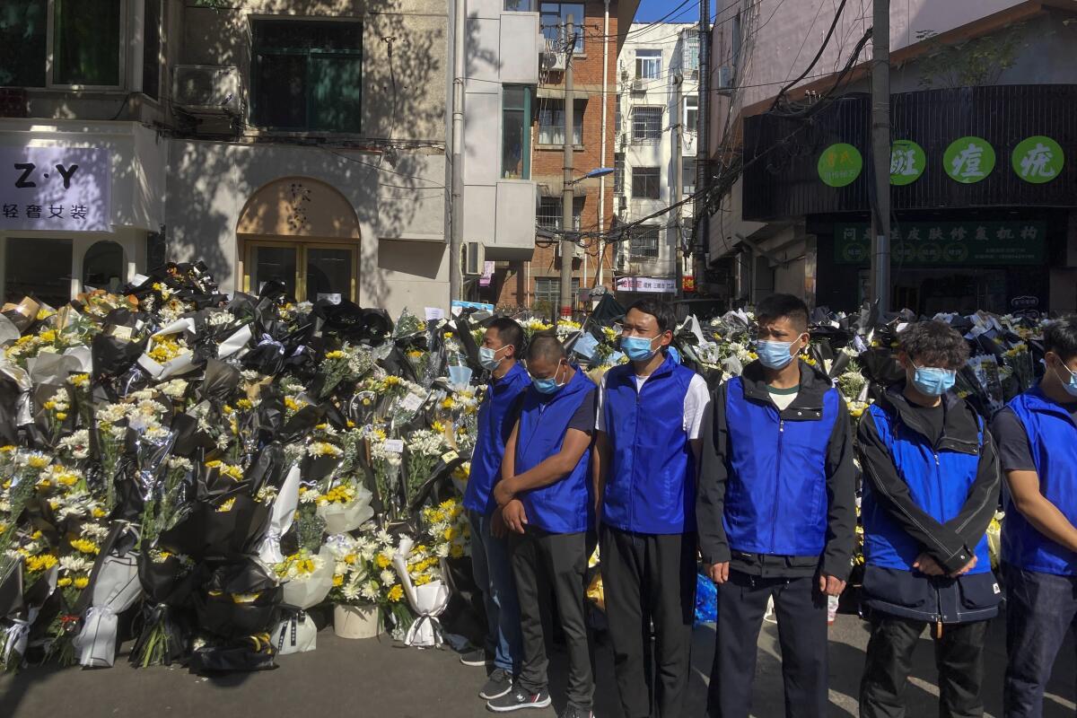Security personnel in blue vests standing in front of flowers laid in memory of former Chinese Premier Li Keqiang