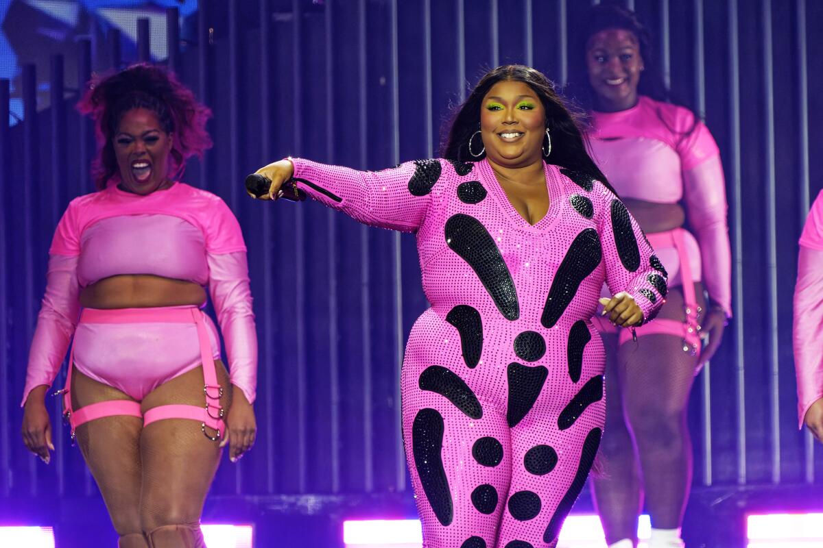 Lizzo wears a pink-and-black jumpsuit onstage alongside female dancers in pink shirts and short shorts  
