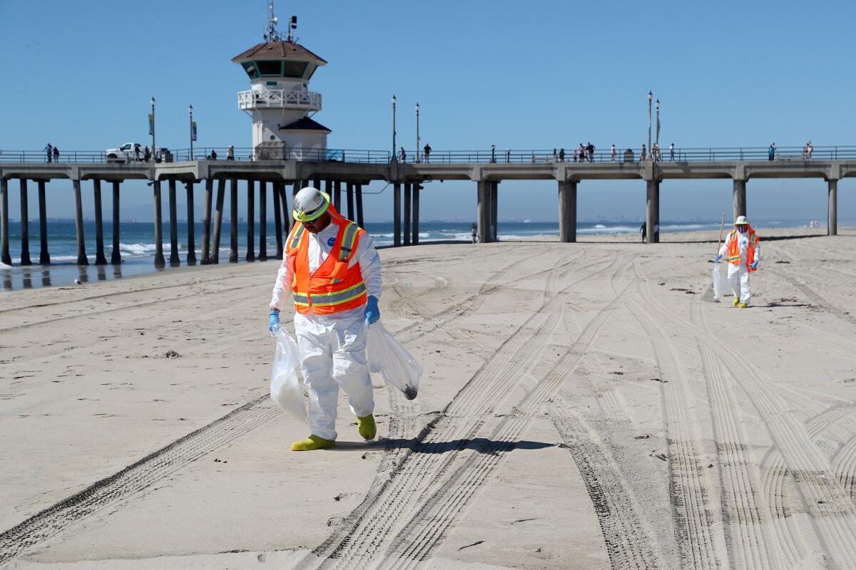 Crew workers search for items to pick up on the south side of Huntington Beach Pier on Tuesday.