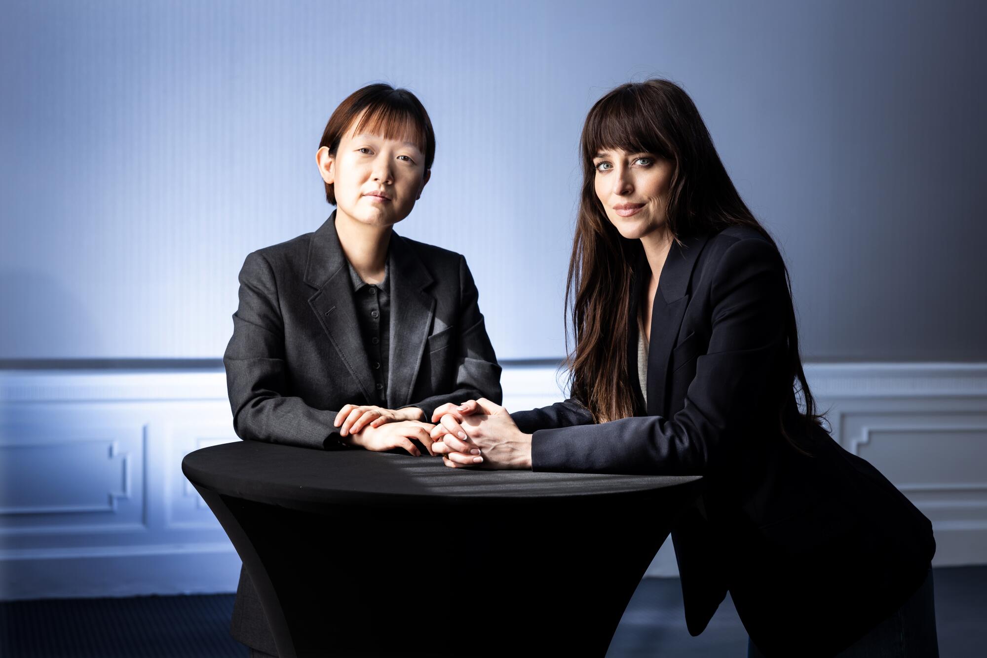 Two women in blazers pose at a cocktail table.