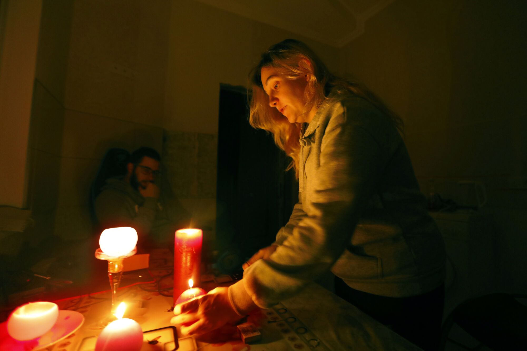 A woman on the right holds one of the lit candles on a table while a man looks on in the background 