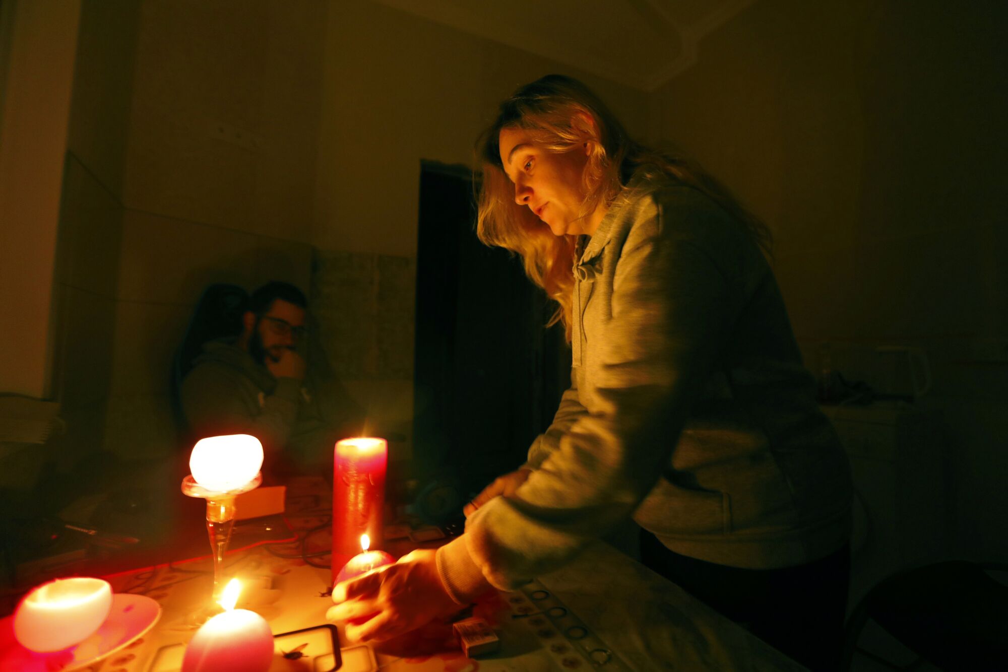 A woman, right, holds one of the lighted candles on a table as a man seated in background watches 