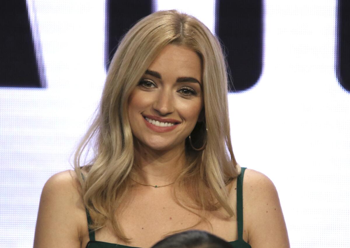 Brianne Howey sits on stage while wearing a green strappy dress.