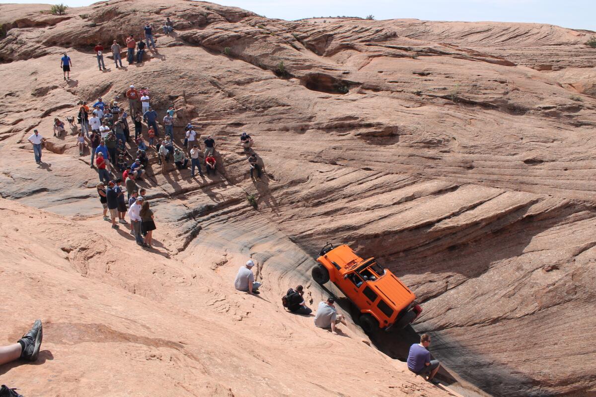 A crowd cheers as an orange Jeep Wrangler crawls to the top of the famous Hell's Gate climb on Hell's Revenge Trail in Moab, UT, during the 48th annual Easter Jeep Safari.
