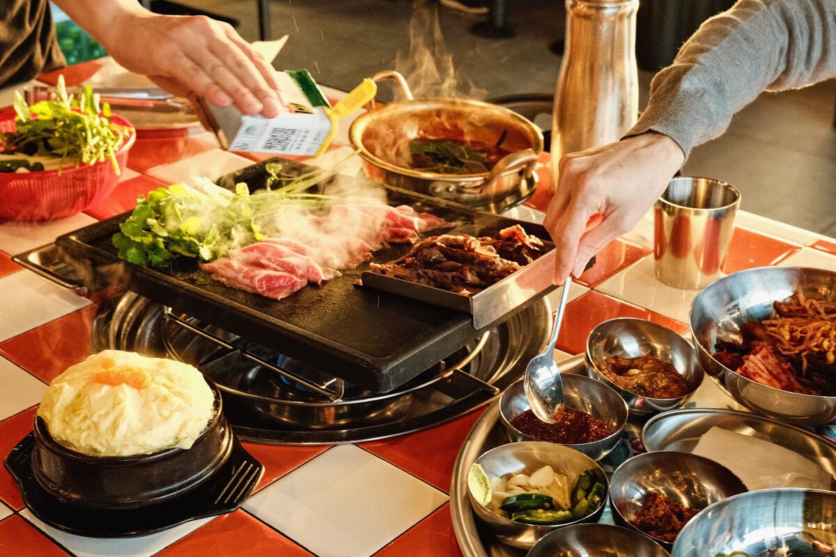 One hand seasons brisket on the grill at K-Team BBQ in Koreatown, while another spoons banchan.