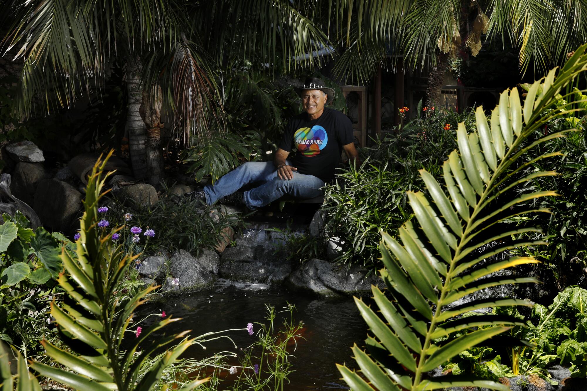 A man sits among plants and trees.