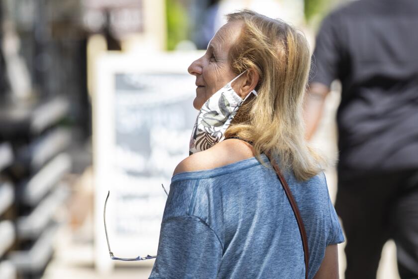 Redondo Beach, CA - May 14: A woman's mask hangs around one ear, not covering her face, while she walks along S. Catalina Avenue in the Riviera Village shopping area of Redondo Beach, CA, a day after the Centers for Disease Control and Prevention (CDC) loosened guidelines for vaccinated people, with masks no longer being necessary when outdoors or in most indoor situations, Friday, May 14, 2021. The new guidelines state that fully vaccinated people no longer need to wear a mask or physically distance in any setting, except where required by federal, state, local, tribal, or territorial laws, rules, and regulations, including local business and workplace guidance. (Jay L. Clendenin / Los Angeles Times)