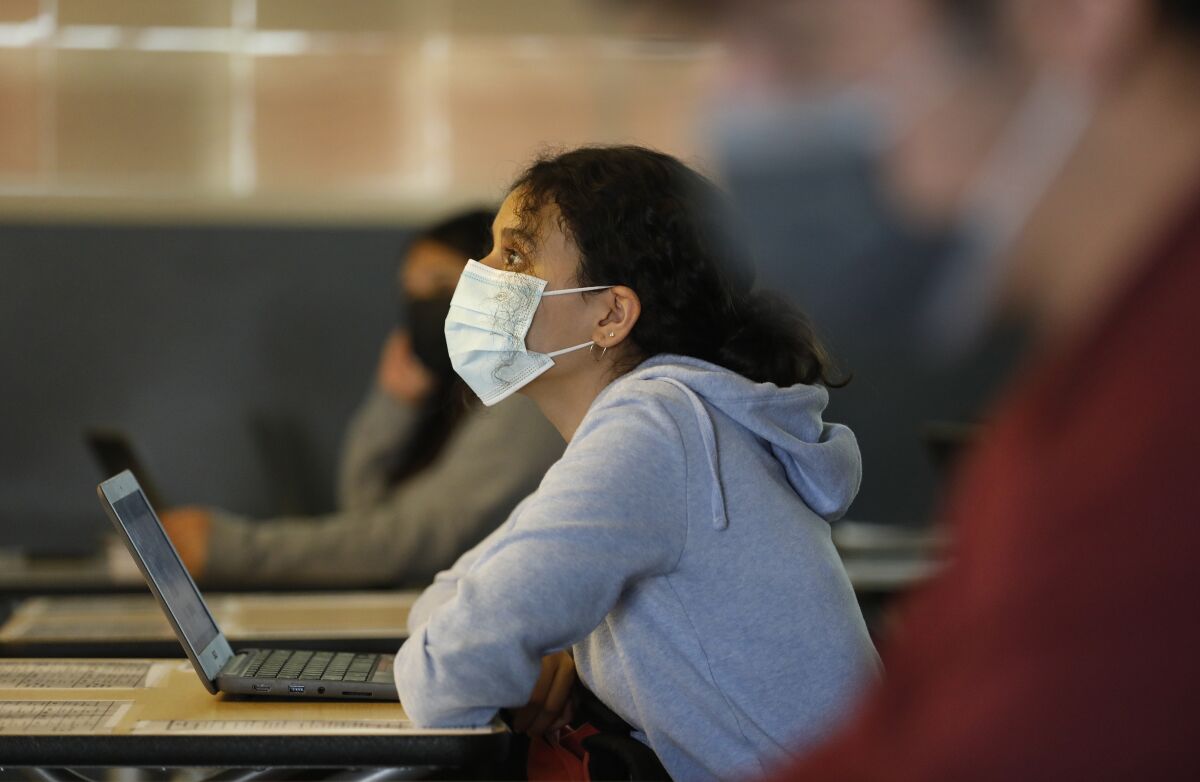 A student with a laptop wears a mask in class. 