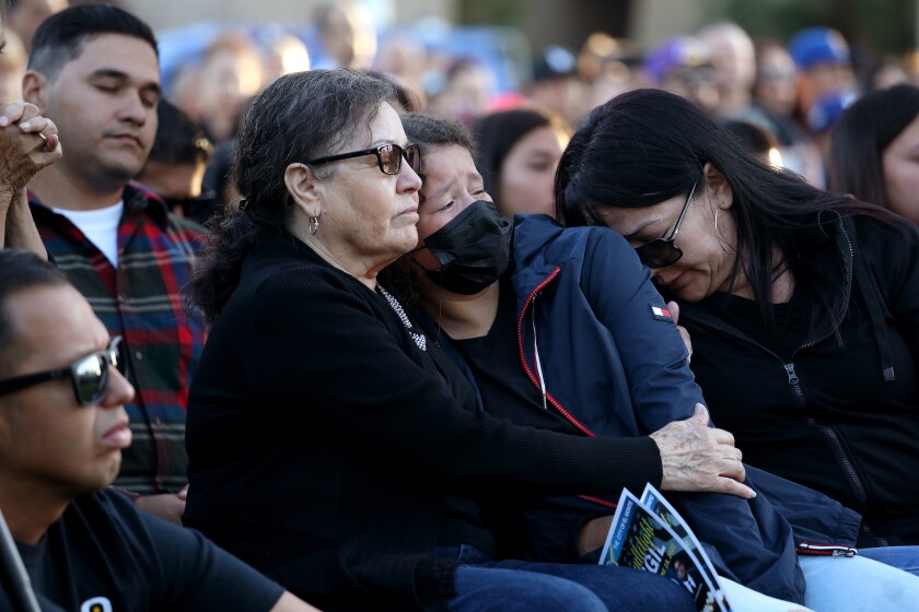 A girl in a face mask cries as she sits between two women among the crowd