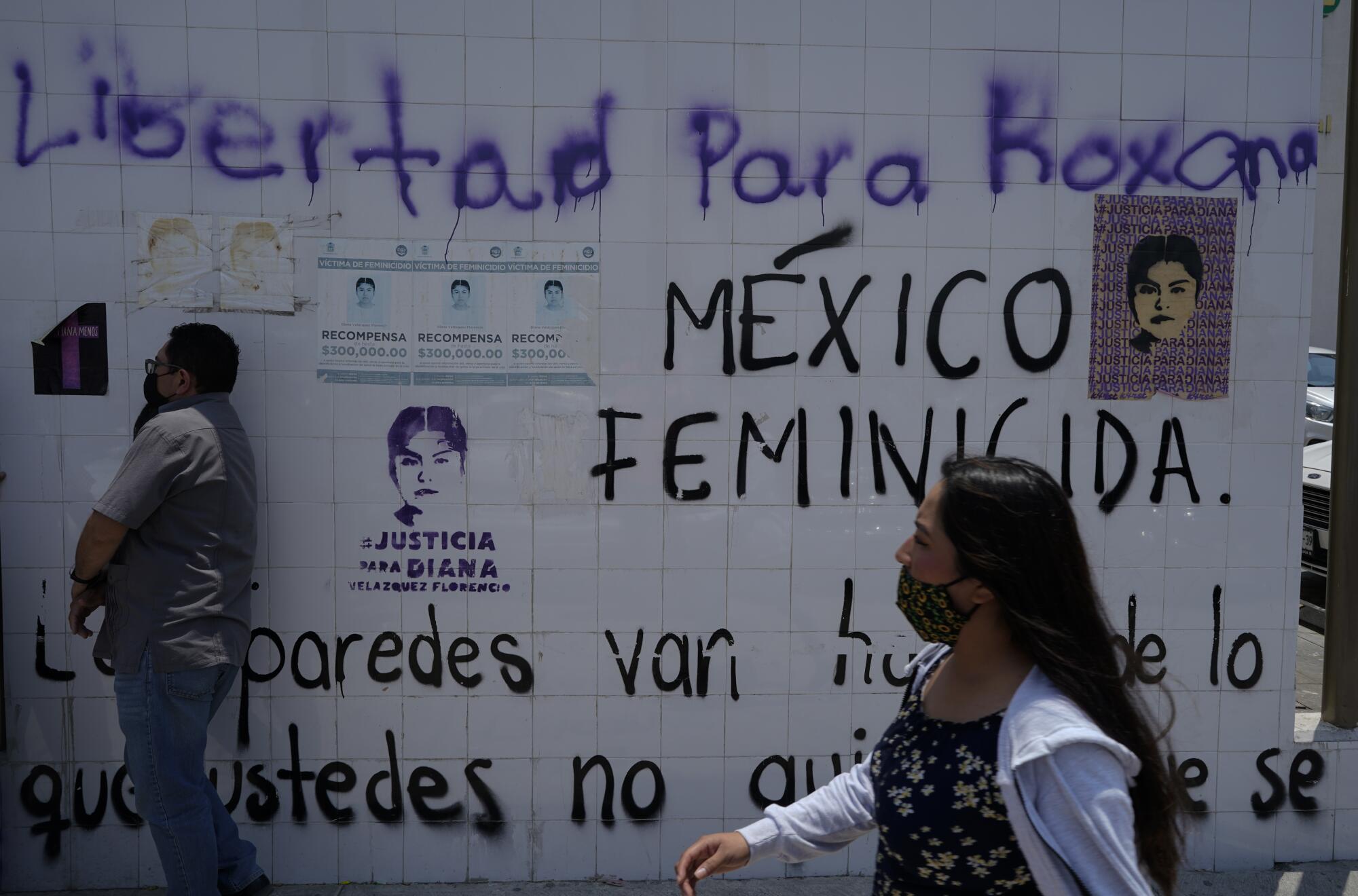 People pass a white wall bearing messages in Spanish