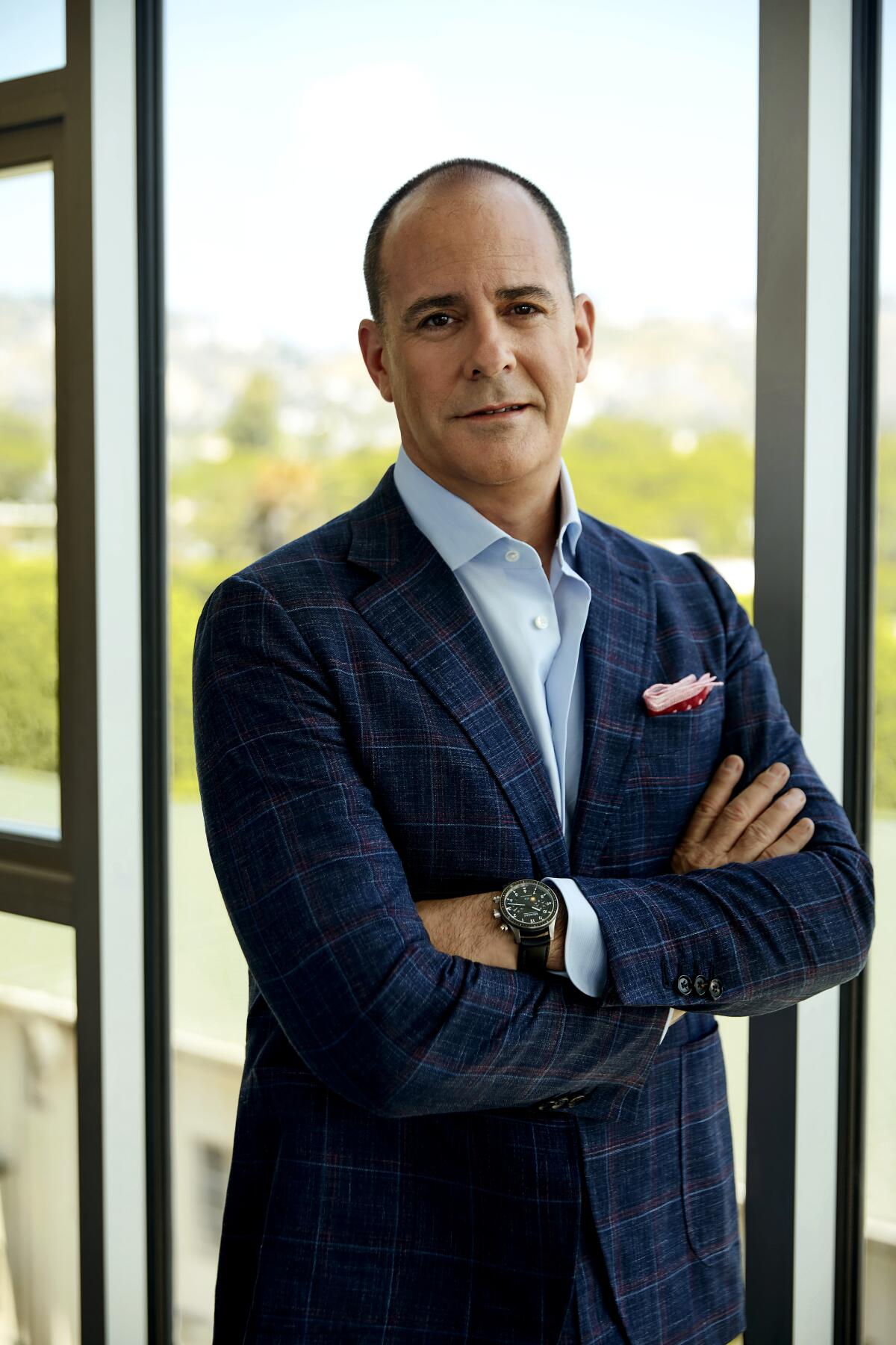 David Nevins, in a suit, stands with his arms folded.