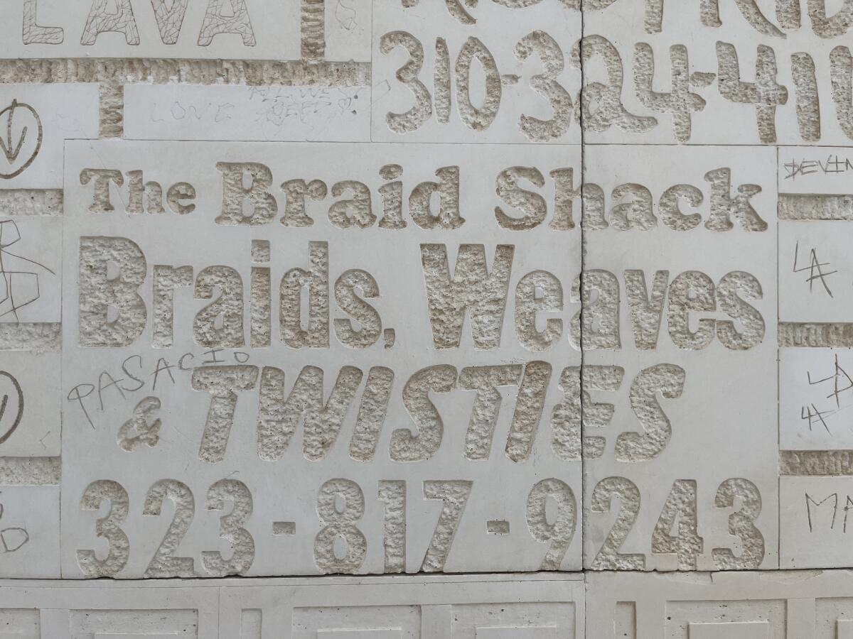 Carved into a wall is a phrase from a sign that reads "The Braid Shack: Braids, Weaves & Twisties"
