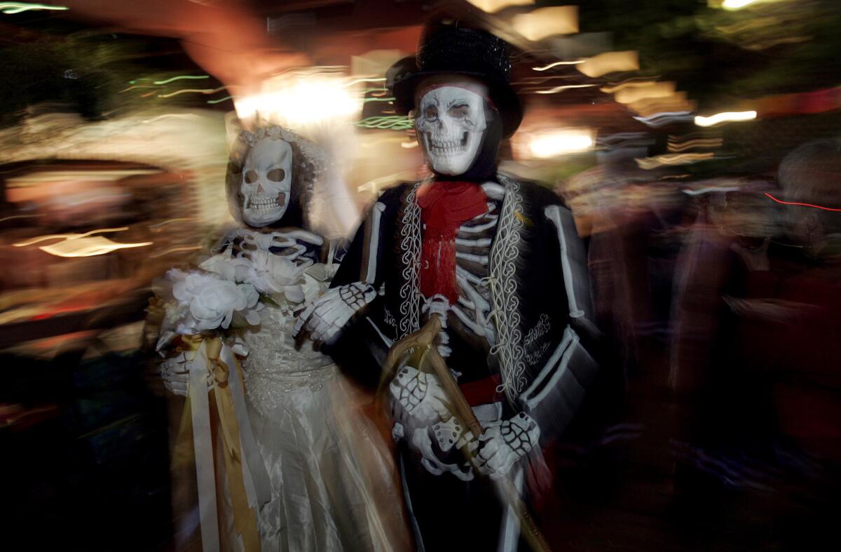 Yamilleth Perez, left, and Lester Galindo, of Pico Rivera, play the bride and groom in a small persession down Olvera Street during a Dia de los Muertos event.