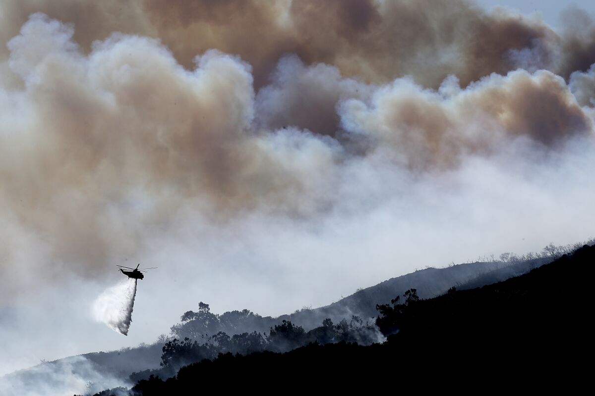A gigantic plume of smoke billows above a firefighting helicopter in the burn zone of the Alisal fire near Goleta.