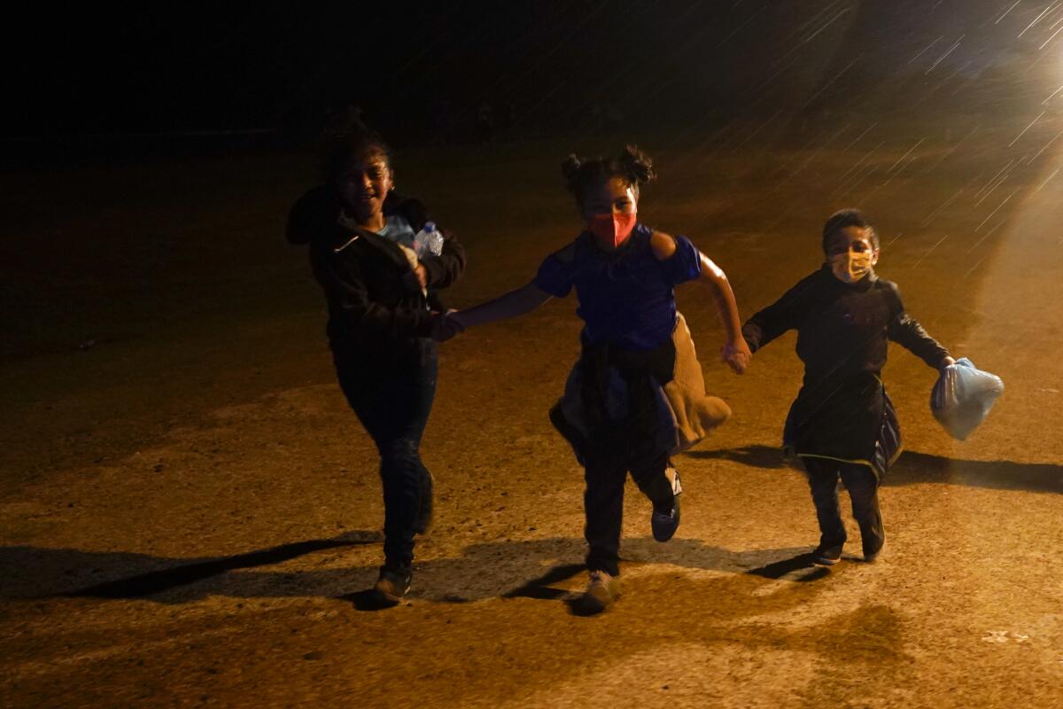 Three young children hold hands as they run in the rain