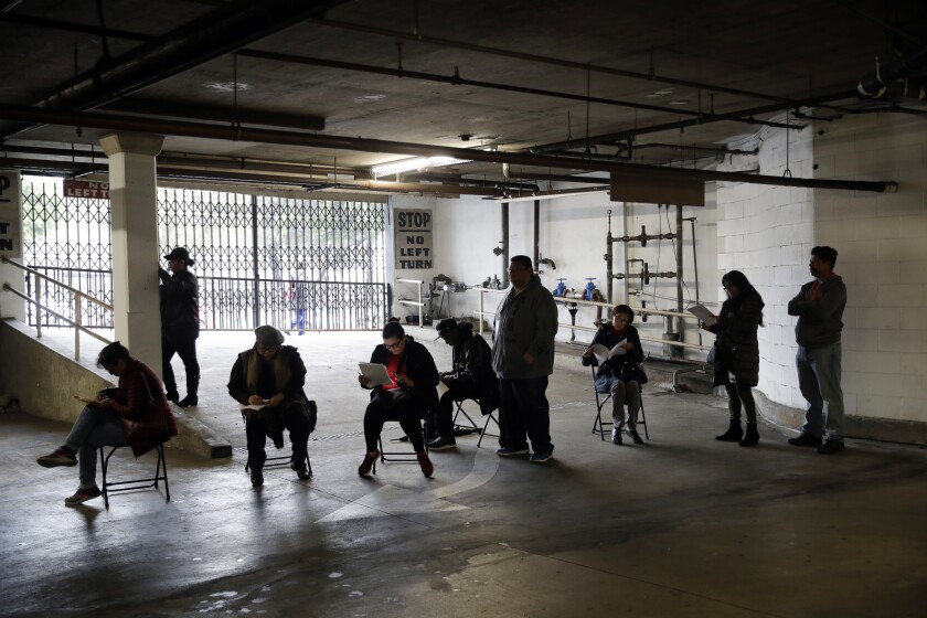 People wait in line inside a parking structure holding paperwork.