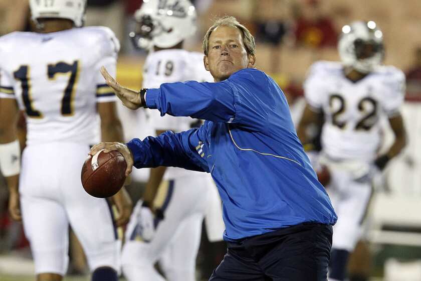 UCLA Coach Rick Neuheisel, a former Bruins quarterback, throws a pass as his players warm up for their game against USC on Saturday evening at the Coliseum.
