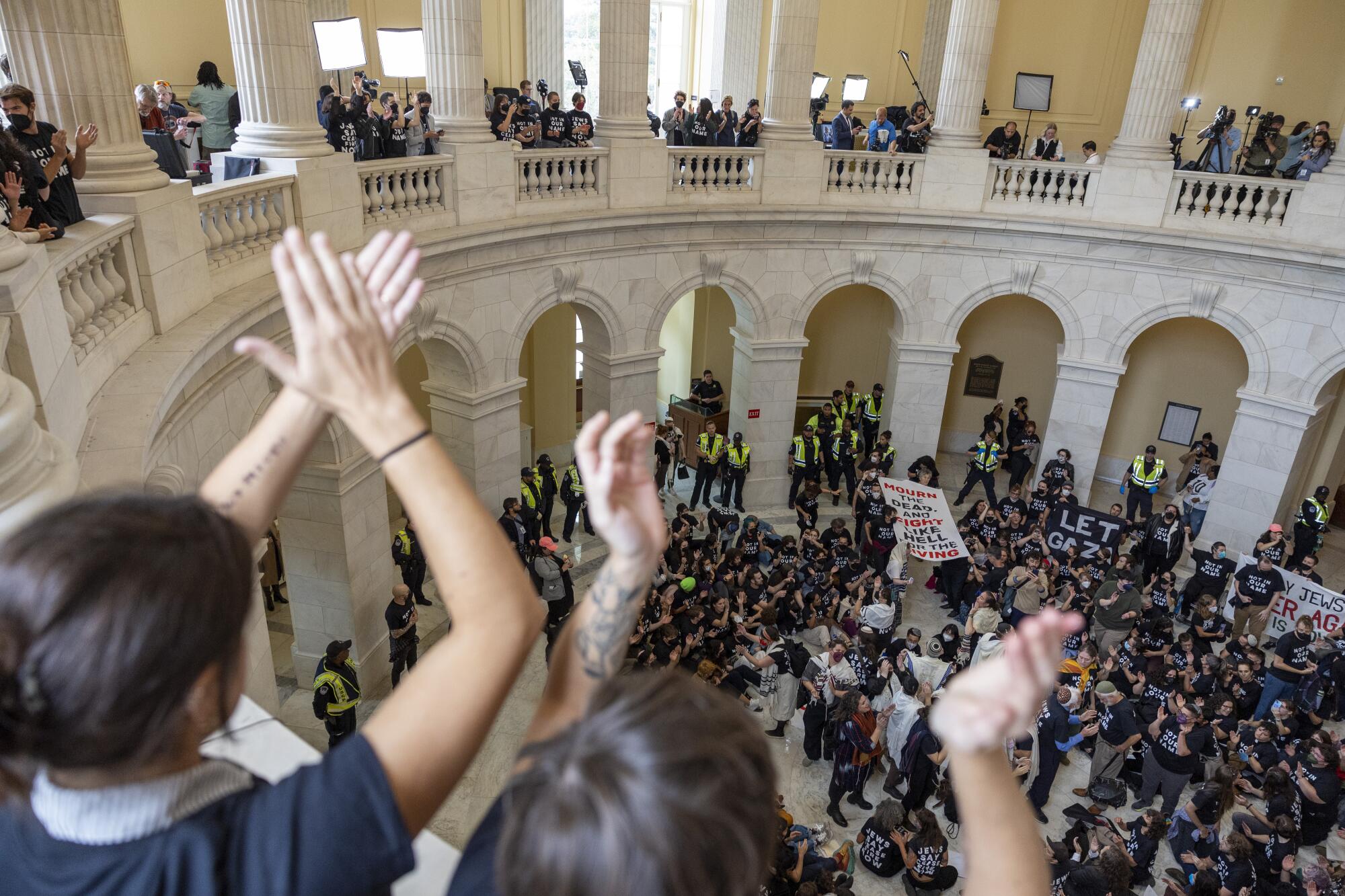 People of hold up their hands in a rotunda with white pillars and balustrades