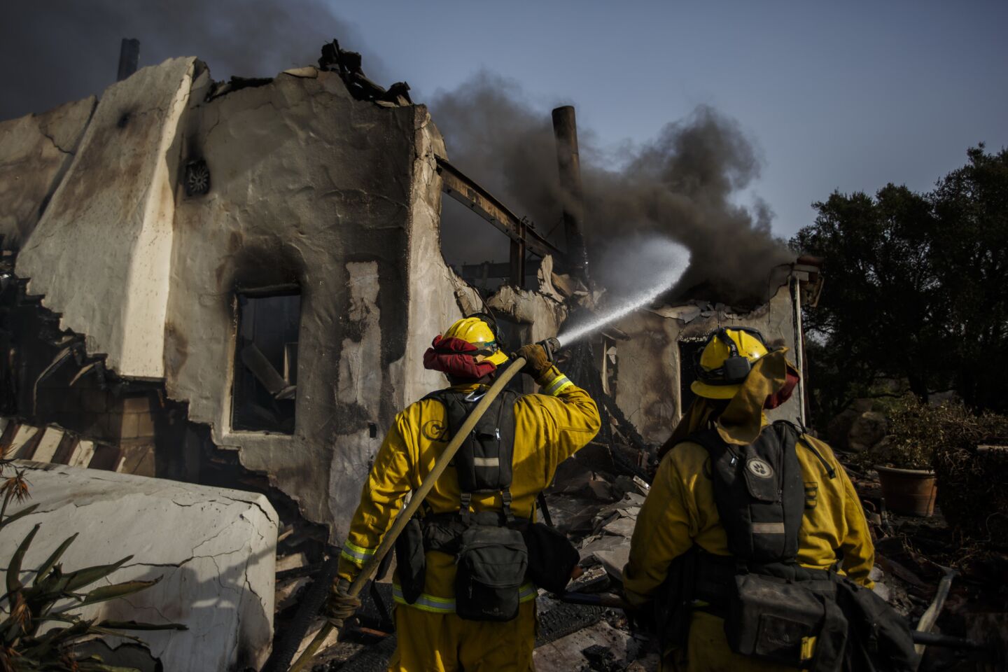 Humboldt County firefighters Bobby Gray, left, hoses down smoldering flames inside a destroyed home, as Kellee Stoehr, right looks on, after the Thomas Fire burned in Montecito, Calif. on Sunday.
