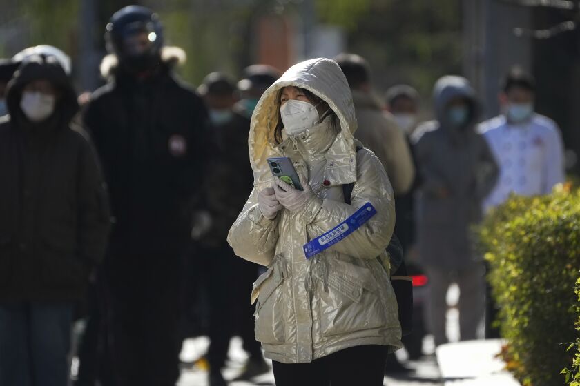 A woman walks by residents in line for their routine COVID-19 tests in cold weather near the site of last weekend's protest in Beijing, Wednesday, Nov. 30, 2022. China's ruling Communist Party has vowed to "resolutely crack down on infiltration and sabotage activities by hostile forces," following the largest street demonstrations in decades staged by citizens fed up with strict anti-virus restrictions. (AP Photo/Andy Wong)